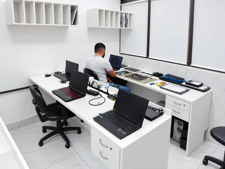 Laboratório da SSTech com notebooks nas bancadas e um técnico trabalhando ao fundo