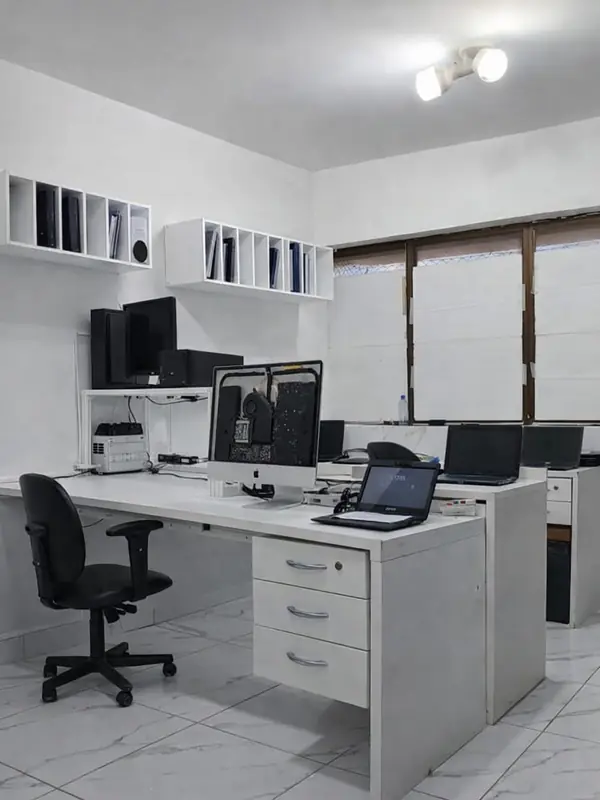 Laboratório da SSTech: bancada branca com um computador aberto para manutenção e notebooks nas mesas ao fundo