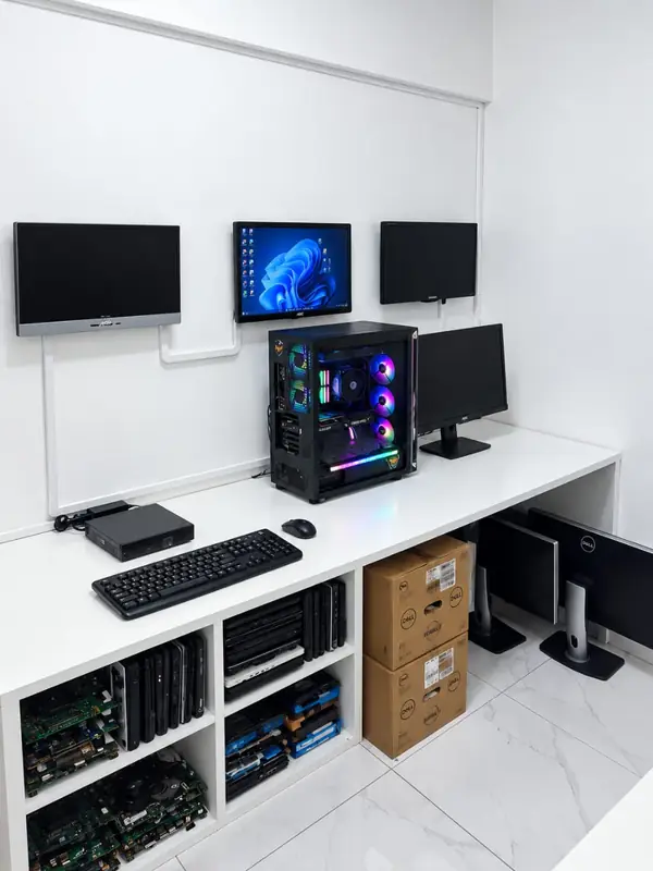 Laboratório da SSTech: bancada branca com monitores na parede, um computador e prateleiras com placas e notebooks